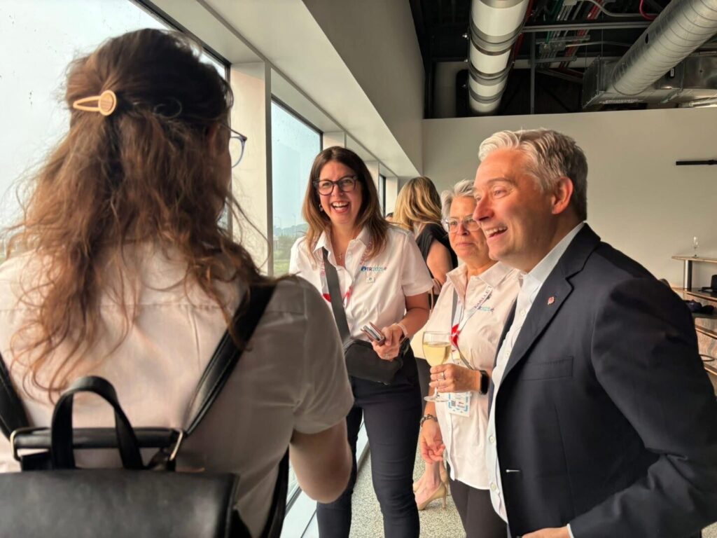 Lors de la soirée d'inauguration des Jeux du Québec à Trois-Rivières, notre fondatrice (au centre, riant) échange avec François-Philippe Champagne, ministre de l’Innovation, des Sciences et de l’Industrie du Canada. L’ambiance est conviviale dans cet espace lumineux surplombant la ville.